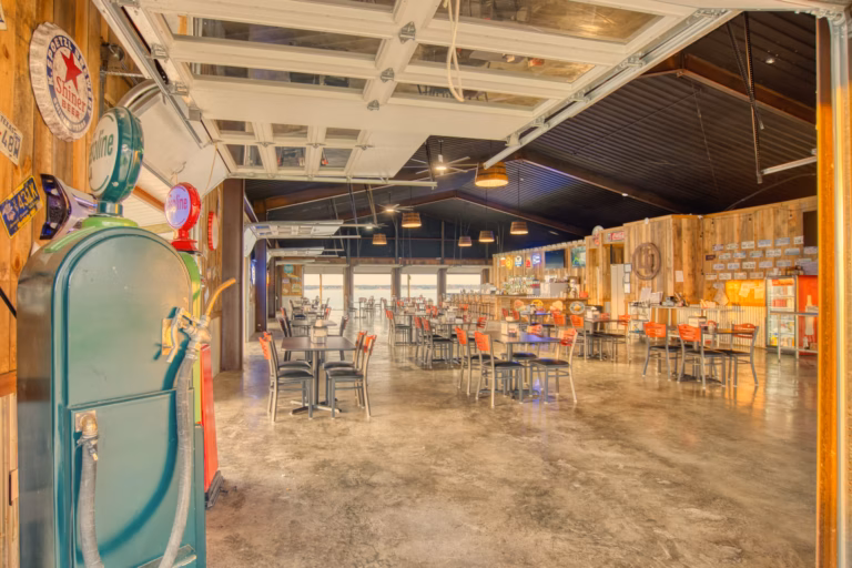 Spacious retro-themed restaurant with industrial decor, metal chairs and tables, exposed ceiling, neon signs, and vintage memorabilia on wood-paneled walls.