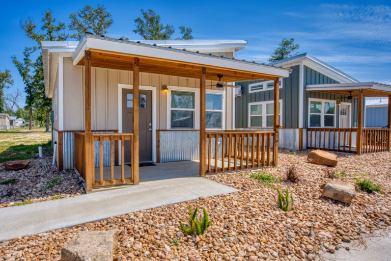 Small modern house with a metal roof, wooden porch, and gravel landscaping under a blue sky.